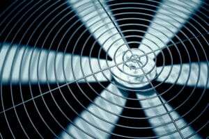 Close-up of a spinning HVAC condenser fan behind a protective metal grille