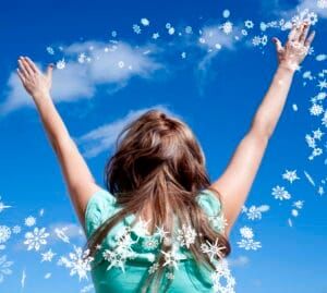 Woman outdoors with arms raised toward a bright blue sky, surrounded by illustrated snowflakes symbolizing fresh, cool air