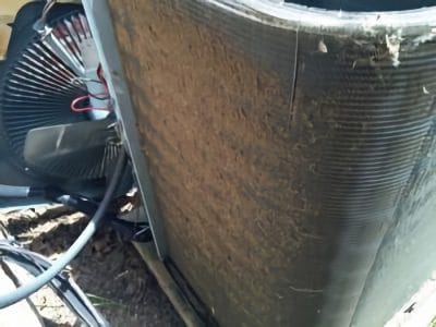 Outdoor air conditioner unit with dirty condenser coils covered in debris, indicating the need for cleaning and maintenance