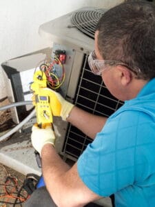 HVAC technician testing an air conditioning unit with a digital manometer to check refrigerant pressure and system performance