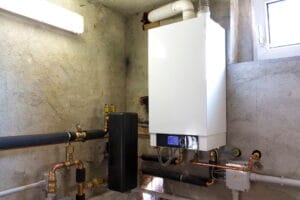 Modern wall-mounted boiler system installed in a concrete basement, connected to copper and PVC piping for home heating and hot water.