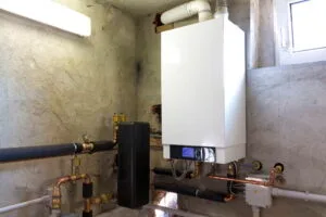 Modern wall-mounted boiler system installed in a concrete basement, connected to copper and PVC piping for home heating and hot water.