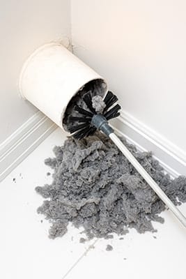 Dryer vent or air duct being cleaned with a rotary brush, surrounded by removed dust and lint debris