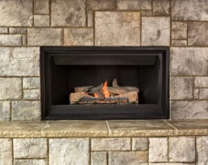 A burning natural gas fireplace surround by stone