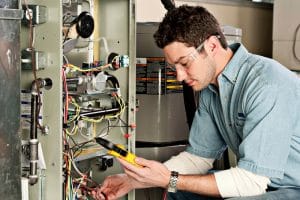 HVAC technician testing wiring inside a furnace during a heating system inspection or repair