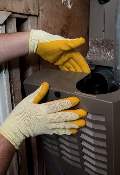 Technician wearing yellow gloves opening a furnace panel for maintenance or heating system repair