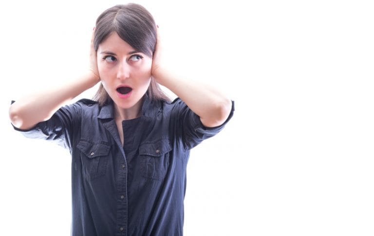 Woman covering her ears with both hands and looking surprised or startled by a loud noise against a white background